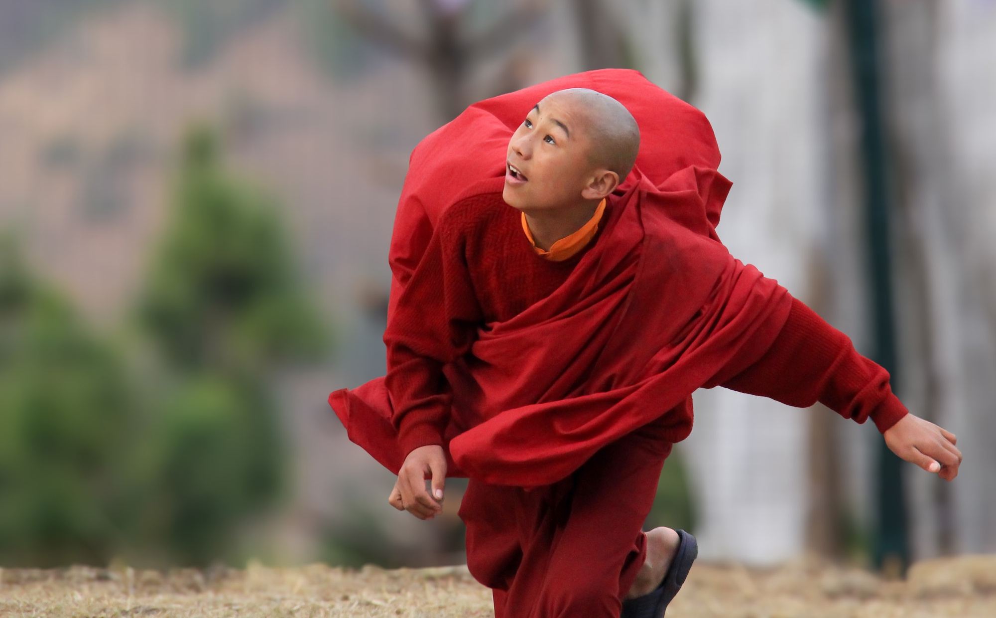 Young Buddhist monk in red robes running across a field